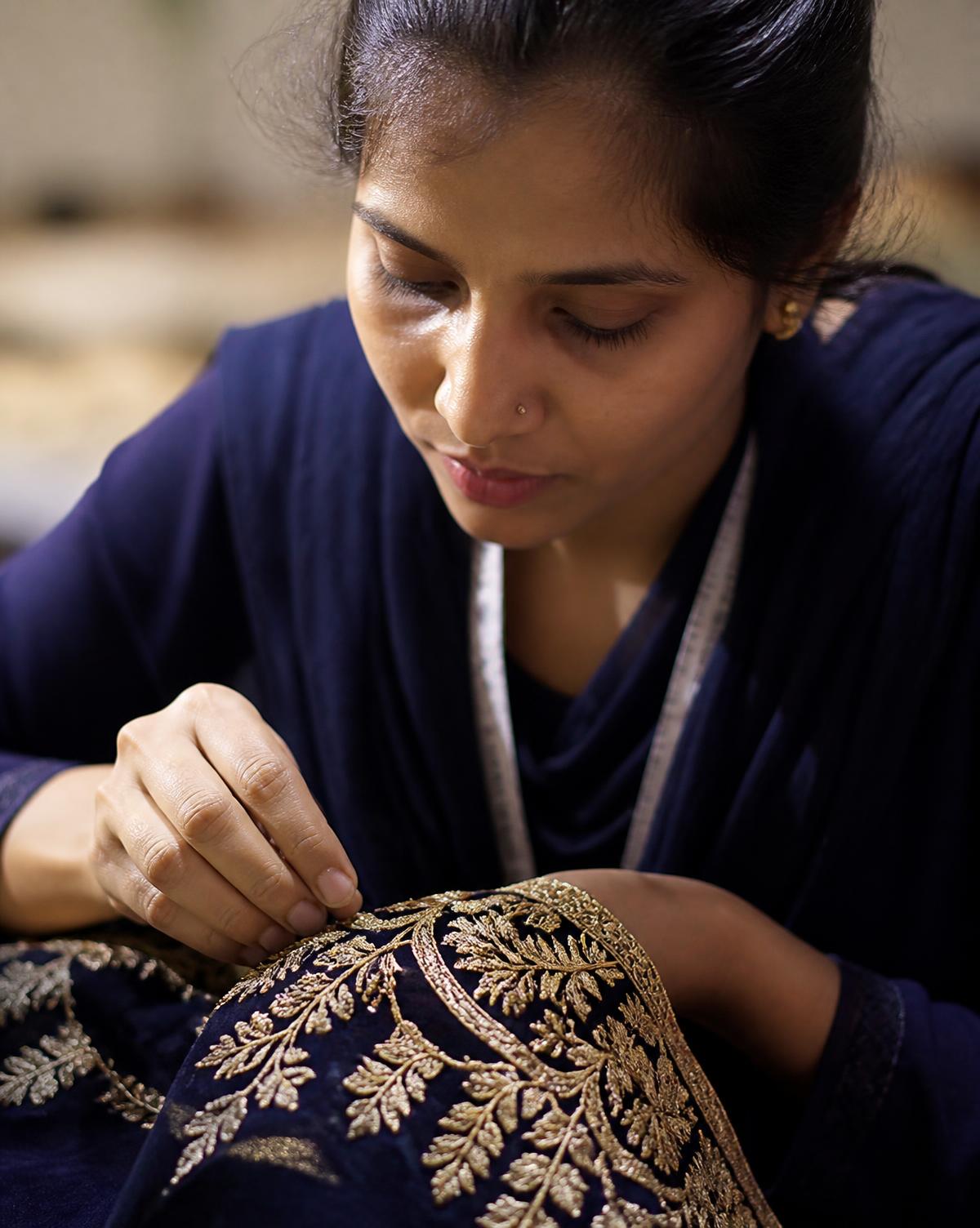 A craftsperson finishing gold embroidery on navy fabric